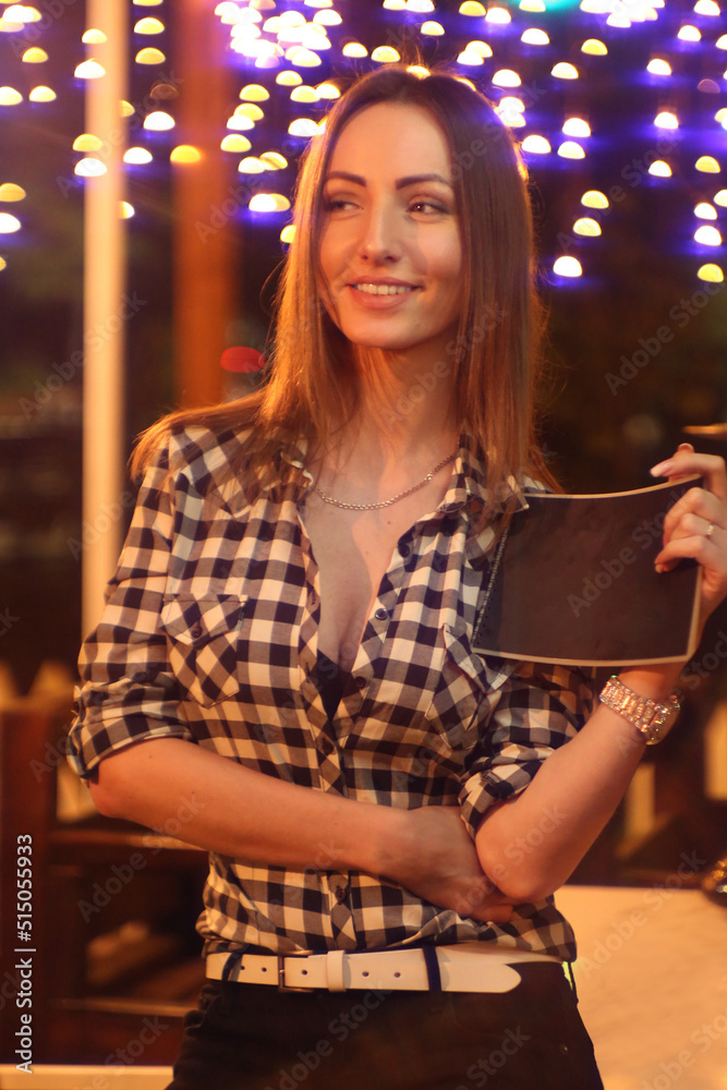 beautiful fashionable girl in a plaid shirt is keeps menu  against the background of lanterns