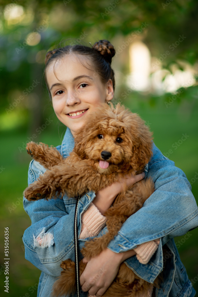 A cute teen girl on a walk with toy poodle dog. It's spring outside. The girl is dressed in a blue jacket in a flower and jeans. Childhood. Pets. A cute teen girl on a walk with toy poodle dog. It's spring outside. The girl is dressed in a blue jacket in a flower and jeans. Childhood. Pets.