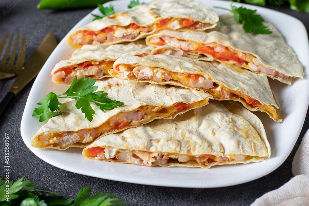 Mexican snack quesadilla from tortilla with bacon, chicken, cheese and pepper in white plate on dark gray background