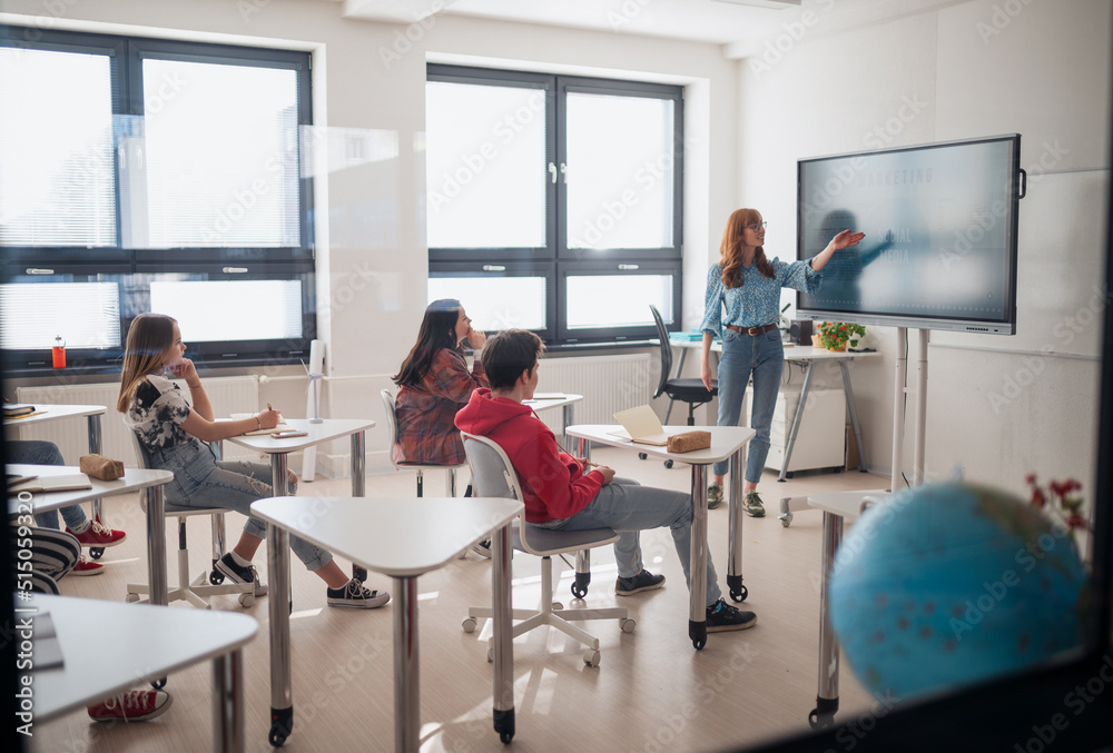 Young High school teacher giving marketing lesson to students in classroom Young High school teacher giving marketing lesson to students in classroom