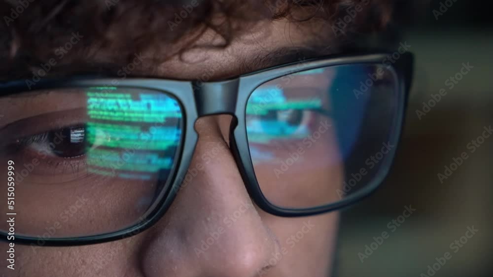 Focused indian developer coder wears glasses working on computer looking at programming code data cyber security digital tech reflecting in spectacles developing software program, close up view.