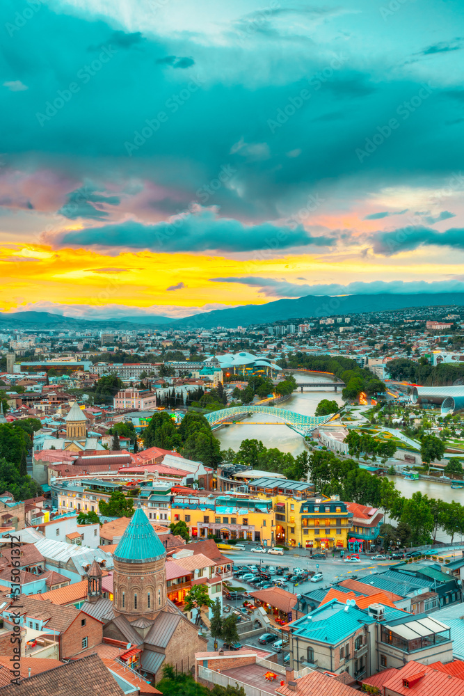The Top View Of Old Colorful Town And Kura Mtkvari River Under Bridges In Summer Tbilisi, Georgia Beautiful Scenic Sunset Sunrise Dawn Cloudy Sky Background.