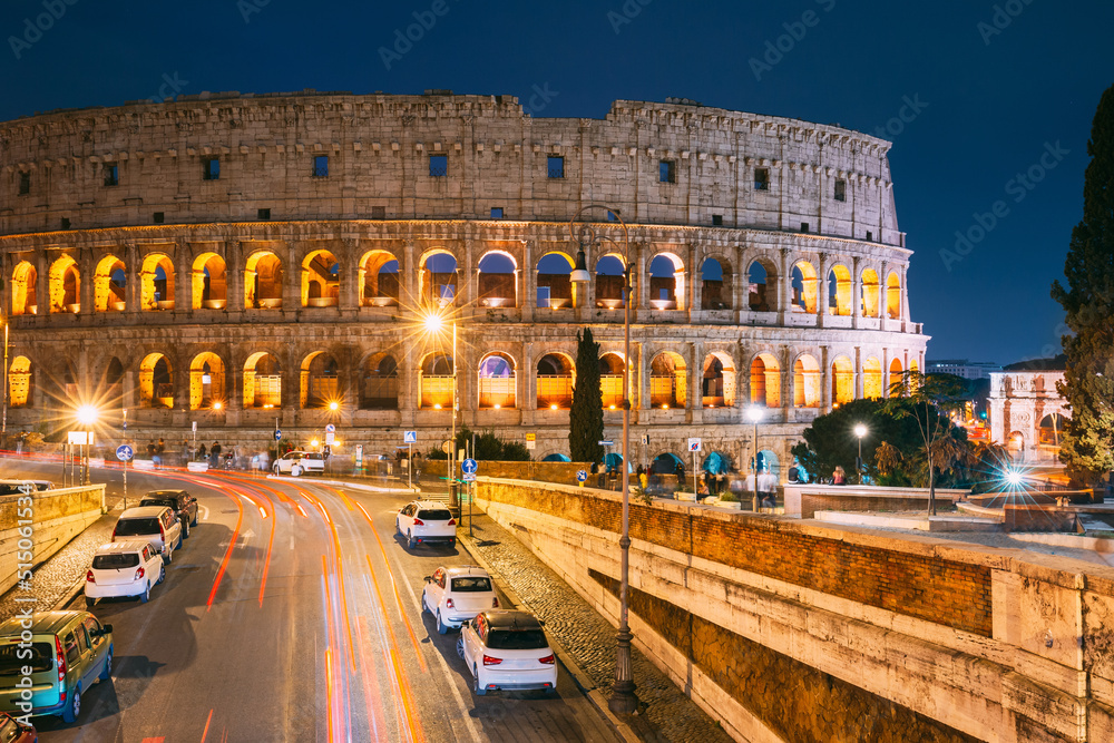 Rome, Italy. Colosseum Also Known As Flavian Amphitheatre In Evening Or Night Time. Night Traffic Light Trails Near Famous World Landmark.