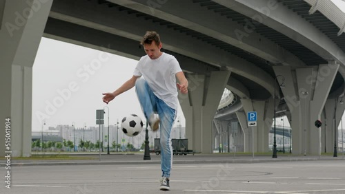 Caucasian teenager man in white T-shirt and blue jeans football freestyler juggles soccer ball, shows various tricks with ball, Professional football player professionally owns juggles ball in city. photo