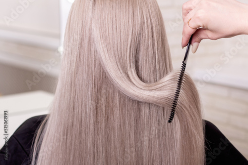 Hairdresser's hand brushing long silver blonde hair in beauty salon 
