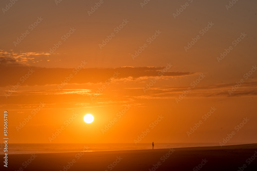 Man walking on the beach in golden sunset with the sun over the sea