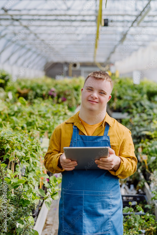 Young man with Down syndrome working in garden centre, holidng clipboard and checking plants. Young man with Down syndrome working in garden centre, holidng clipboard and checking plants.
