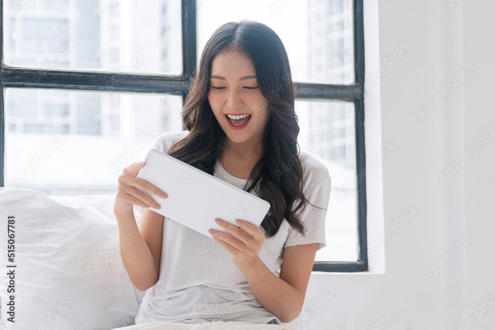 Excited asian woman play gaming online with tablet sitting beside window at home.Joyful young girl holding tablet touchpad playing game application fun relaxed with pillow indoors.Lifestyle technology Excited asian woman play gaming online with tablet sitting beside window at home.Joyful young girl holding tablet touchpad playing game application fun relaxed with pillow indoors.Lifestyle technology