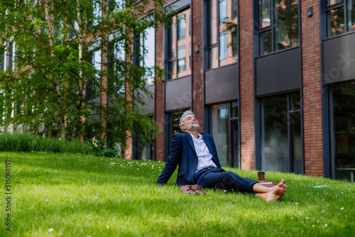 Mature businessman resting and sitting barefoot in park, feeling free, escaping from work, work life balance concept. photo