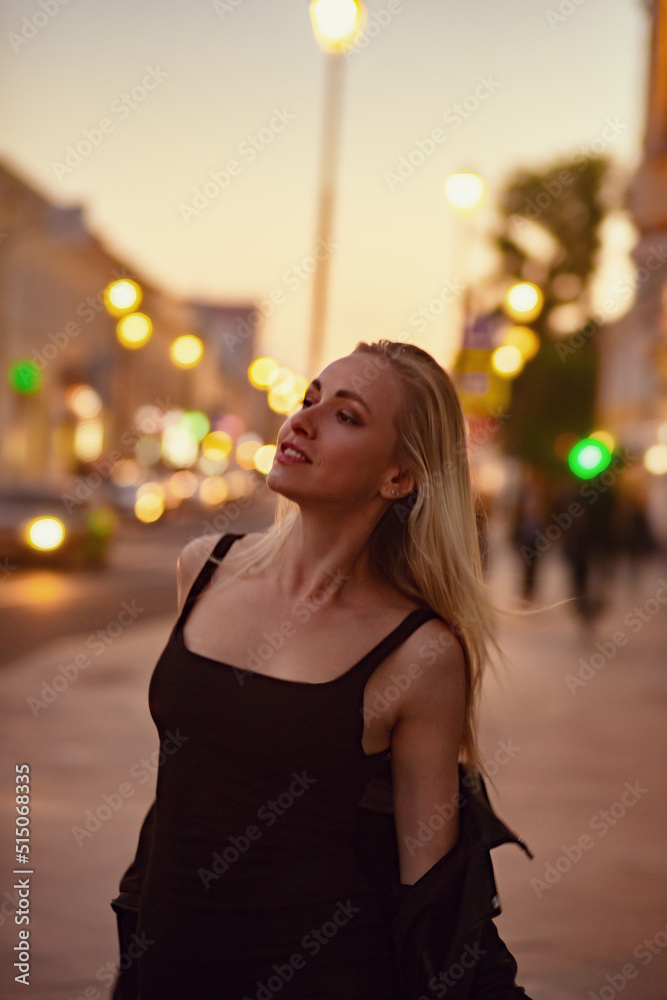 Smiling blond woman posing in fashion style clothes walking on city street summer night lights background. outdoor portrait. Vogue vintage
