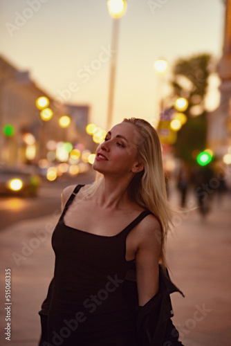 Smiling blond woman posing in fashion style clothes walking on city street summer night lights background. outdoor portrait. Vogue vintage