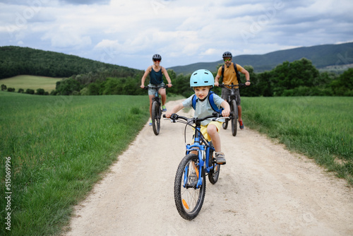 Portrait of excited little boy with his parents at backround riding bike on path in park in summer
