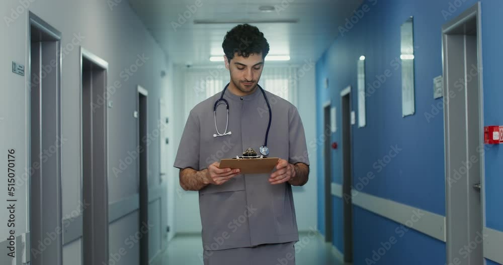 A doctor with a phonendoscope walks along the corridor and looks into a notebook A doctor with a phonendoscope walks along the corridor and looks into a notebook