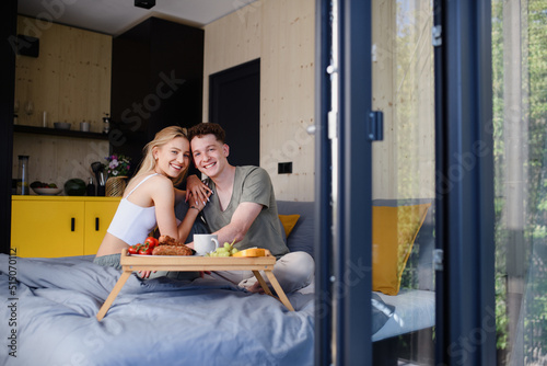 Young beautiful couple in love is sitting in bed and having healthy breakfast together.