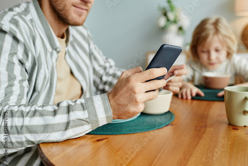 Close up of father using smartphone at dining table with little boy in background, copy space