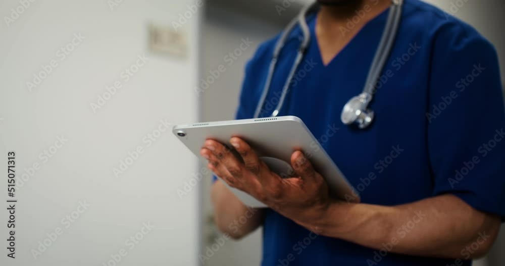 African American doctor uses a tablet standing in corridor of medical center African American doctor uses a tablet standing in corridor of medical center