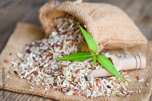 brown rice in the sack with wooden background , raw various rice color mixed thai rice for cooking food , Loonzain rice brown black red white purple health food. photo