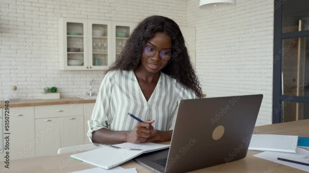 Happy young black woman student learning at home looking at laptop computer watching online webinar, having virtual work meeting or elearning training seminar class on video call digital conference.