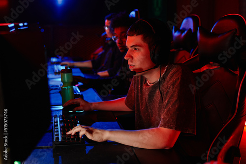 Side view portrait of young man playing video games in eSports club lit by red neon