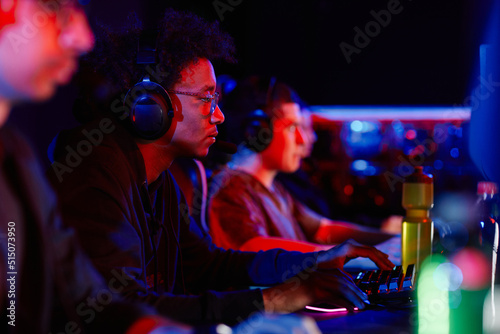 Side view portrait of young black man playing video games with cyber sports team in neon light