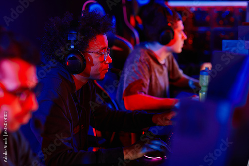 Side view portrait of young black man playing video games with diverse eSports team in neon light