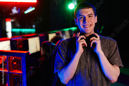Waist up portrait of young man on cyber sports team smiling at camera cheerfully lit by neon light  copy space