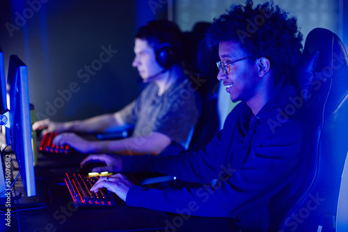 Side view portrait of smiling African American man playing video games in cybersports club in blue neon lighting