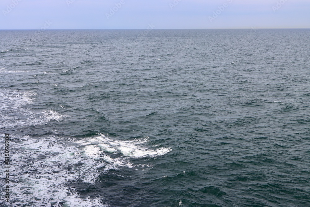 Fototapeta premium Stern waves with white foam tips on greyish blue sea water, photo taken from aboard ship. Selective focus