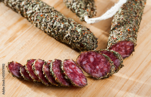 Fotografie Fuet, traditional spanish dry cured sausage with fine herbs on wooden table