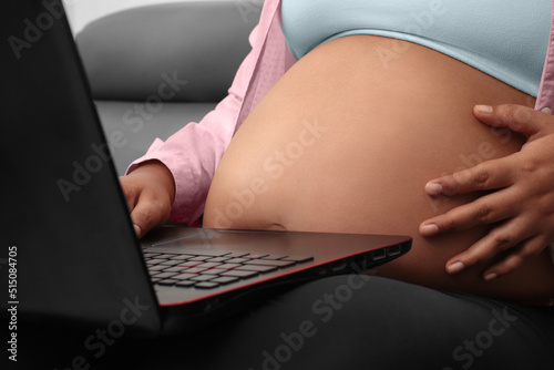 pregnant woman working on laptop sitting on couch in living room