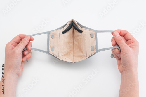 View of hands holding reusable face mask with replaceable filter and adjustable ear loops
