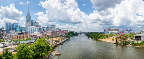 The Cumberland River flows through the city of Nashville, Tennessee, with downtown skyscrapers rising on one bank and a professional football stadium on the other. photo