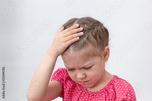 Child with headache holding hand on head on white background caucasian little girl of 5-6 years in red looking down