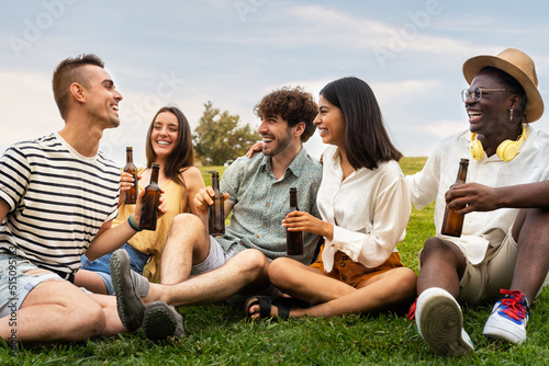 Multiracial friends laughing together enjoying some cool beer outdoors in park. Having fun.