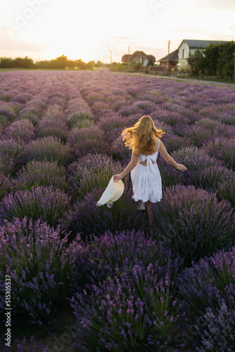 Back view of beautiful girl in a white dress and hat in a lavender field at sunset.