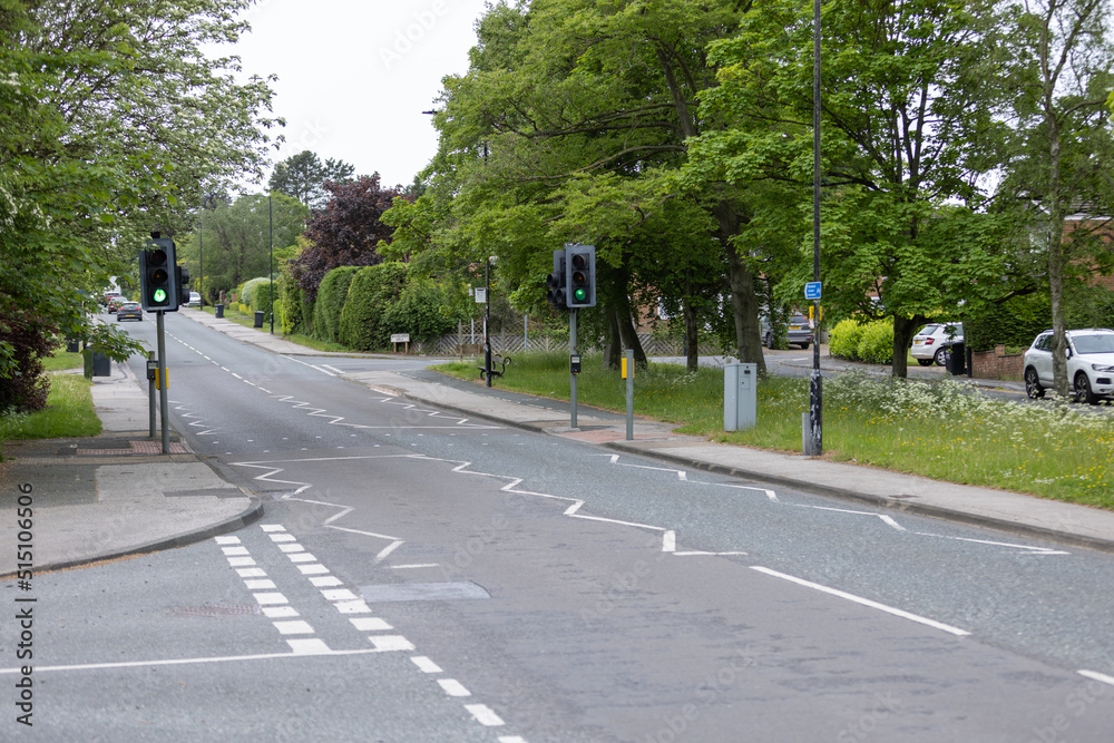 Empty public road in Harrogate, Yorkshire with traffic lights and street markings surrounded by trees