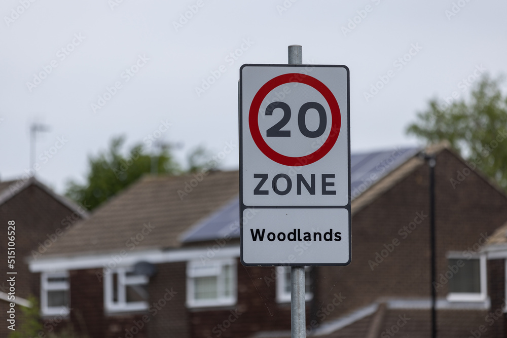 Public speed limit sign at urban area in Harrogate, UK saying 20 zone Woodlands with houses in the background