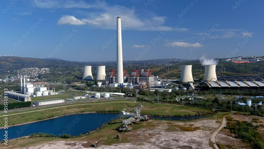 Thermal power plant with smoking chimney behind the lake and old drilling machine, bottom wind turbines on a sunny afternoon. Drone firing traveling forward. As Pontes, Lugo, Spain Thermal power plant with smoking chimney behind the lake and old drilling machine, bottom wind turbines on a sunny afternoon. Drone firing traveling forward. As Pontes, Lugo, Spain