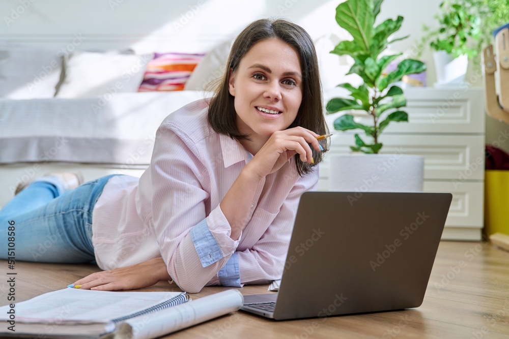 Attractive young woman looking at camera lying on floor at home with laptop Attractive young woman looking at camera lying on floor at home with laptop