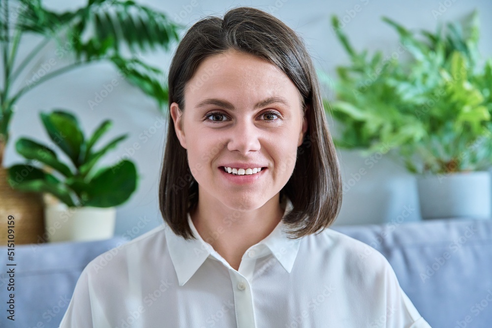 Headshot young smiling woman looking at camera in home interior Headshot young smiling woman looking at camera in home interior