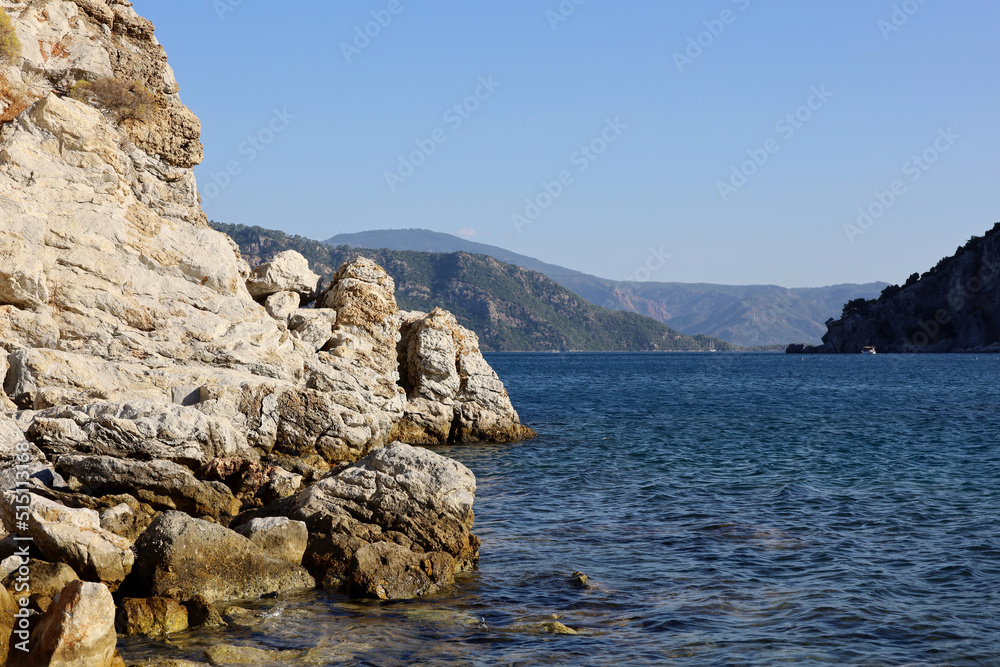 Picturesque view to rock cliff in Mediterranean sea. Summer coast with turquoise transparent water and green mountains