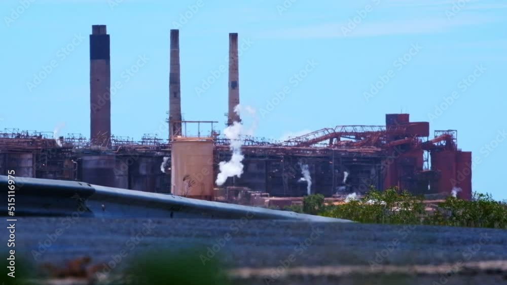 View of large industrial plant from the road with steam coming out and bright blue sky in Central Queensland View of large industrial plant from the road with steam coming out and bright blue sky in Central Queensland