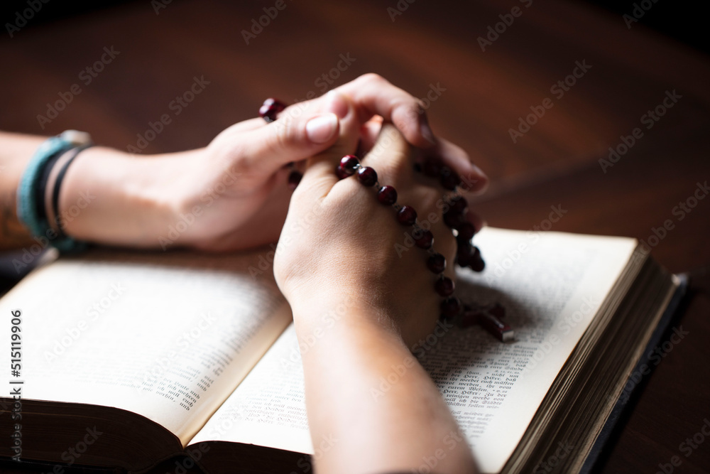 Obraz premium Christianity theme – prayer. Christian woman with Bible praying with hands crossed keeping rosary.