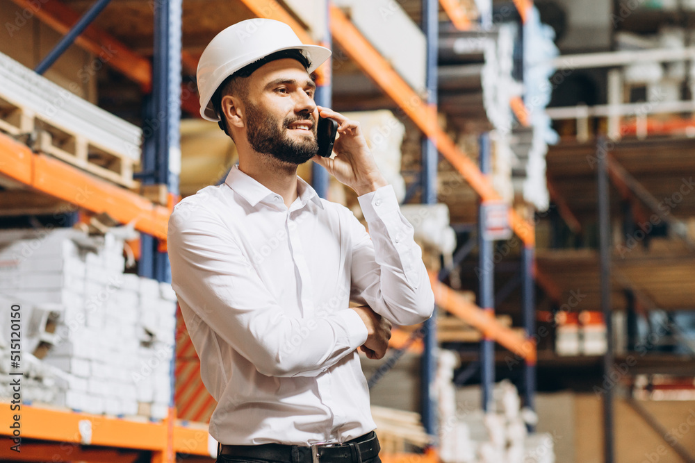 Business man wearing helmet walking in storage and talking on the phone Business man wearing helmet walking in storage and talking on the phone