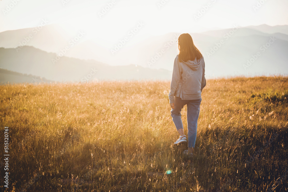 Young Girl in Hoodie Walking in Mountain Golden Field Landscape