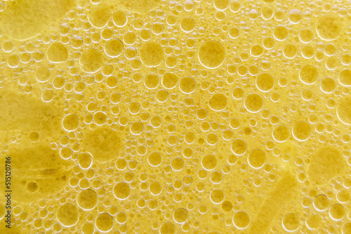 Air bubbles on the surface of the water. Fat rings in an aqueus emulsion. Yellow liquid with bubbles. Horizontal image.