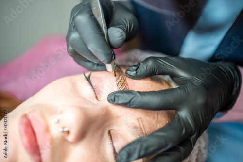 Procedure of eyebrow microblading. A master in black gloves is doing a blending needle of model s brow.