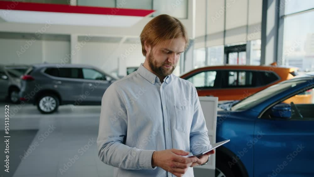 A bearded attractive male manager selects a car on a tablet. Sale at a car dealership A bearded attractive male manager selects a car on a tablet. Sale at a car dealership