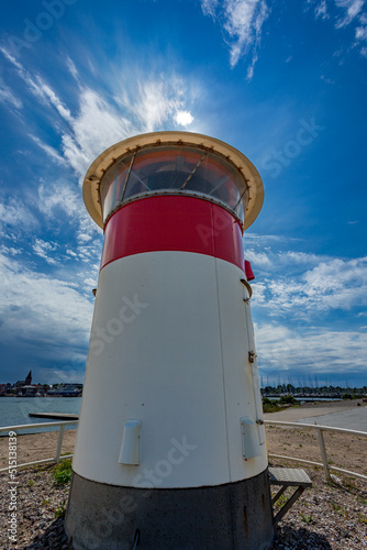 Large red and white lighthouse on a summer day  with path peering against blue sky
