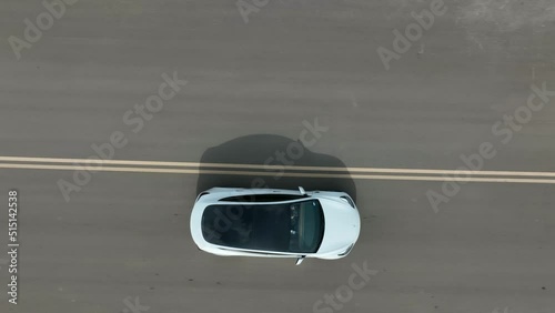 Top down aerial of glass rooftop of Tesla Model 3 driving on open road. Aerial tracking shot. photo